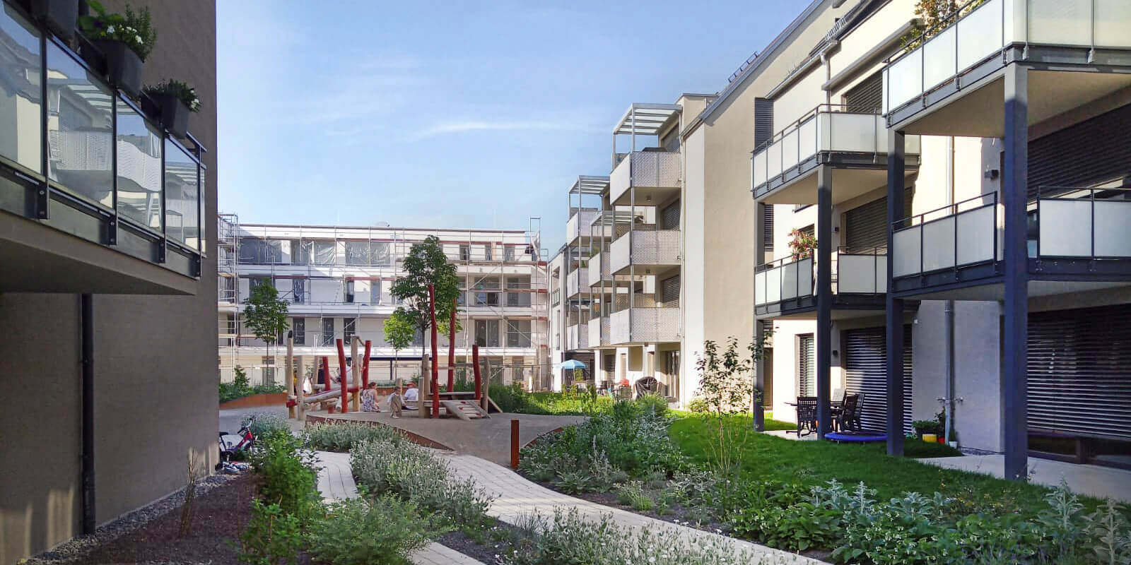 Moderne Wohnanlage mit gestalteter Außenanlage, bepflanzten Wegen und Spielbereich – Beispiel für nachhaltige und nutzerorientierte Freiraumplanung im urbanen Raum.